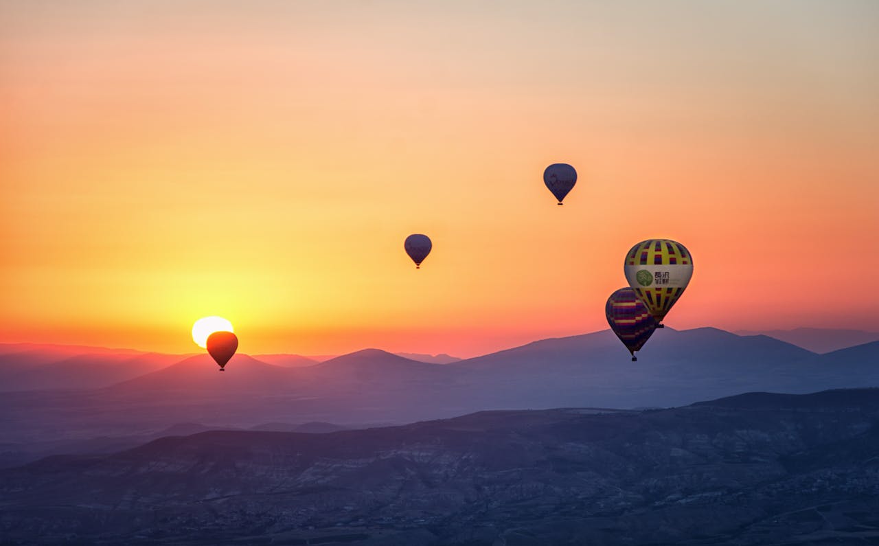 services-bg Stunning view of hot air balloons floating at sunrise over mountainous landscape.