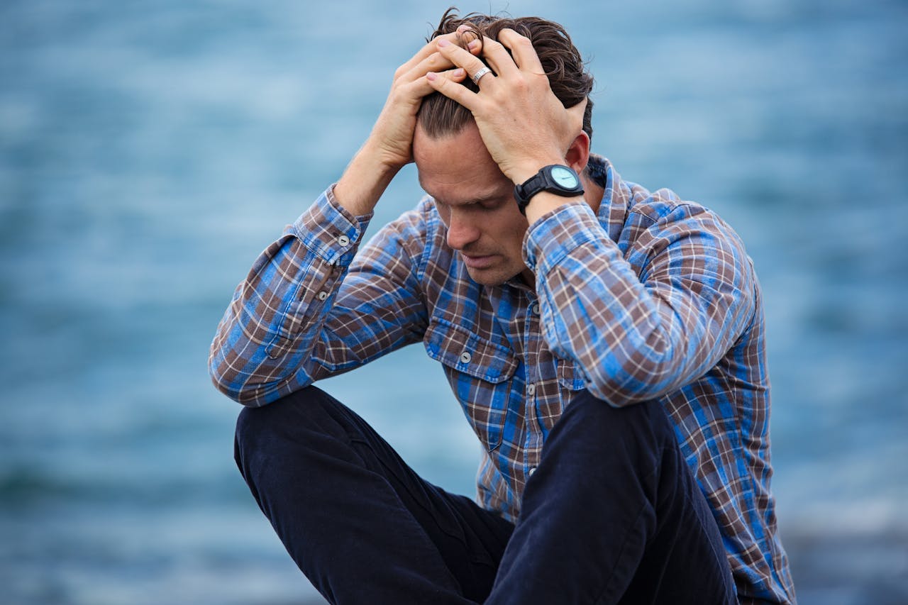 services-04 A man in a plaid shirt sits by the water looking distressed, symbolizing stress.